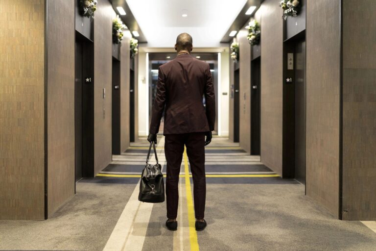 Man in a suit standing with back facing in a elevator lobby.
